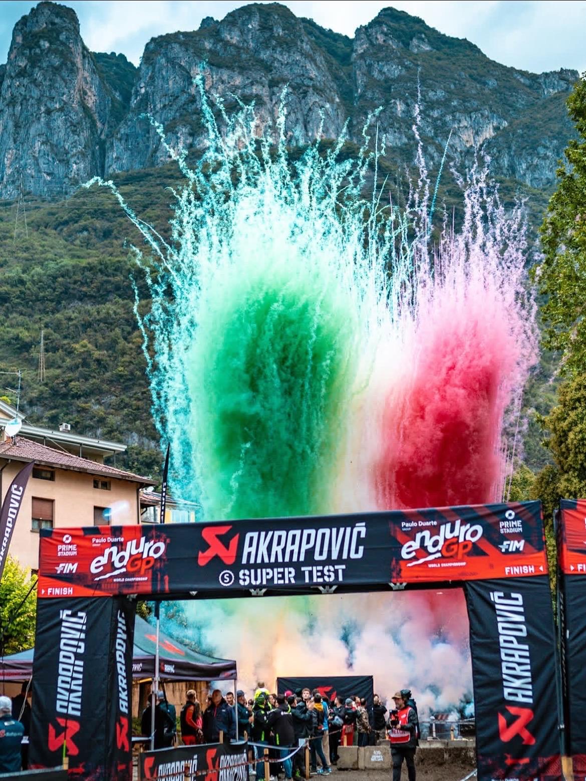 Esplosione di fumo tricolore sopra un evento sportivo con il pubblico alla partenza.